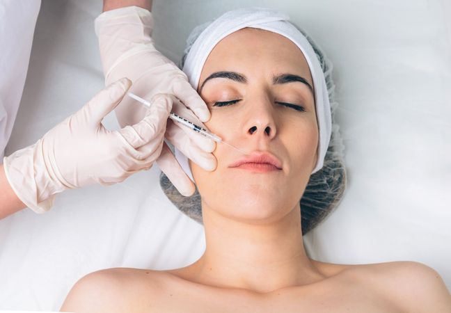 Beautician's hands in latex gloves injecting botox into female's cheek in a beauty salon