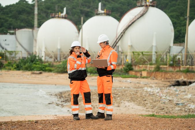 Two engineers are working at an industrial site near spherical gas storage tanks.