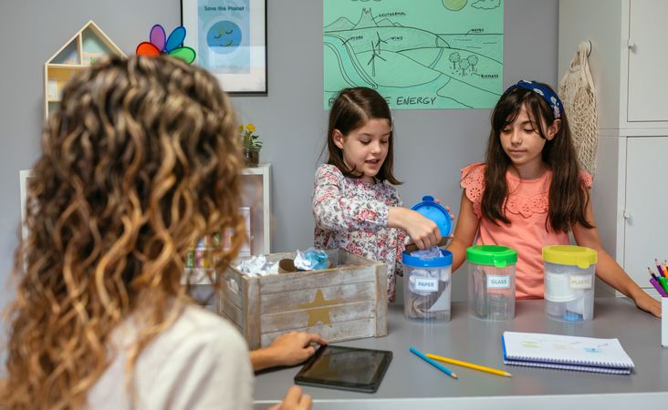 Students showing how to recycle in ecology classroom with her teacher in foreground