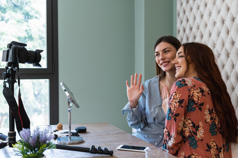 Cheerful young women recording video while sitting at table