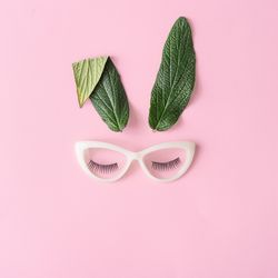 Bunny rabbit face made of natural green leaves with glasses on pastel pink background