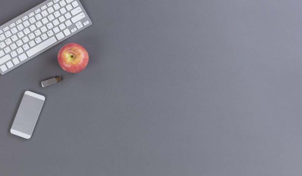 Top view grey desk with keyboard, apple and thumb drive