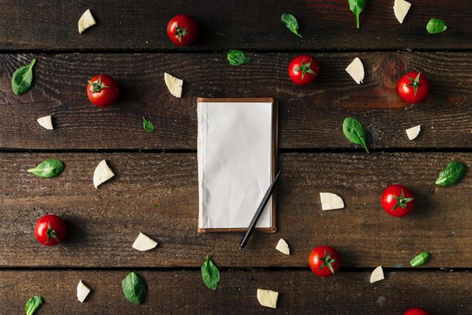 Basil, tomatoes, and cheese on wooden background with notepad