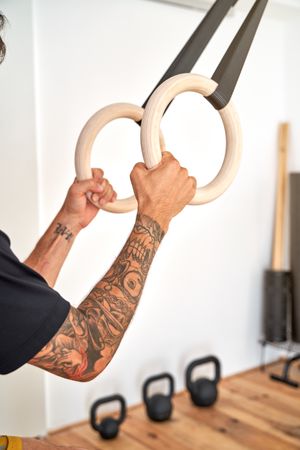 Crop sportsman hanging on wooden gymnastic rings in gym