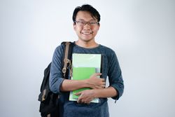 Asian young male student wearing bag and carrying books smiling and happy expression