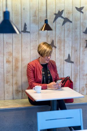 Woman in red coat sitting in cafe texting on phone