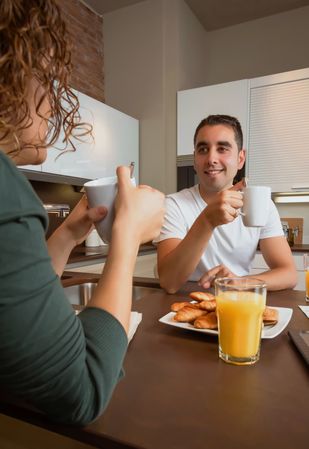 Smiling couple talking while eating pastries and drinking coffee at breakfast