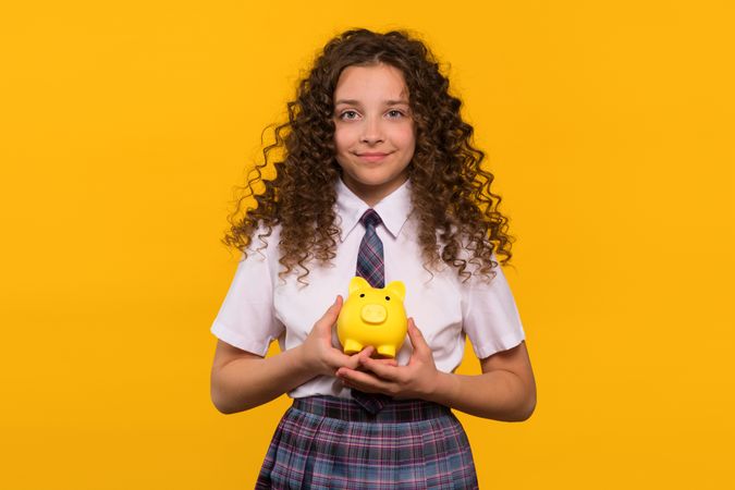 Girl in school uniform holding yellow piggy bank