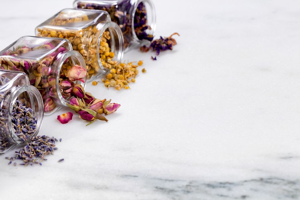 Spices and herbs in small glass jars pouring onto marble stone background