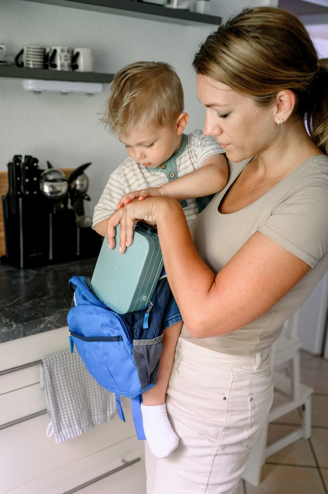 Mother and son standing in kitchen with lunchbox and backpack