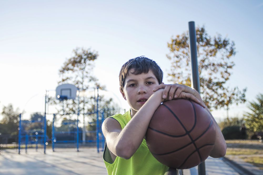 Young teen male standing on a street basket court while smiling at camera