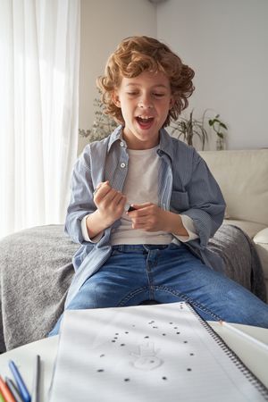Cheerful boy sitting on sofa and drawing picture