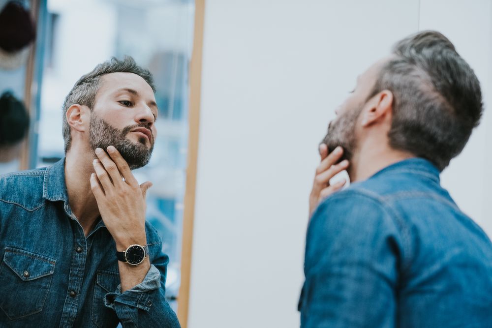 Man looking at mirror and touching beard in salon