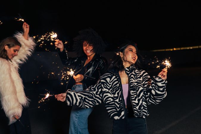 Three women partying   together with sparklers at night