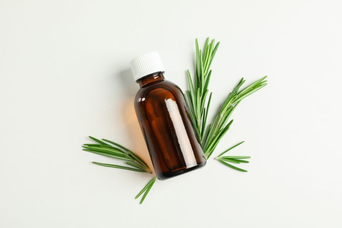 Flat lay composition with rosemary oil and leaves on plain background, space for text
