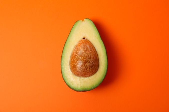 Half of fresh avocado on orange background, close up