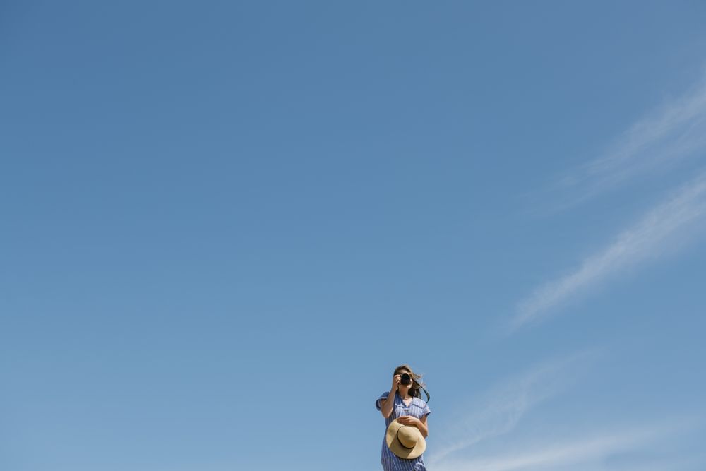 Traveling young female taking photo against blue sky