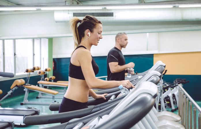 Side view of two people jogging on gym treadmills