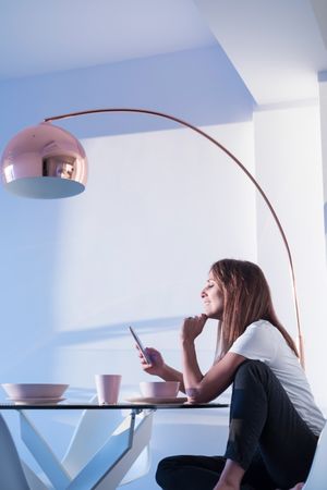 Woman sitting at breakfast table checking phone in front of cereal bowl