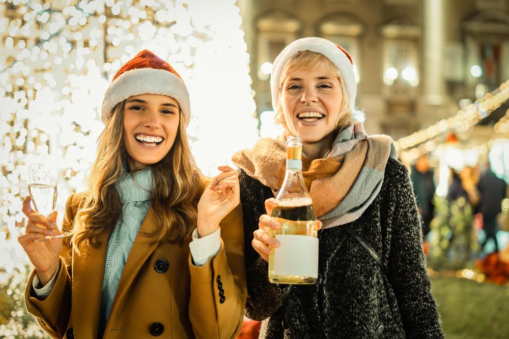 Two happy young women in Santa hats celebrating with champagne and looking at the camera.