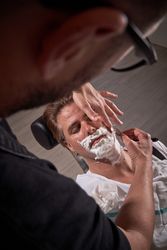 Unrecognizable barber shaving beard of man in chair