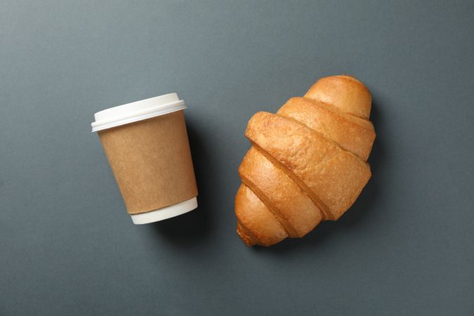 Freshly baked croissant and takeaway coffee on dark grey background, top view
