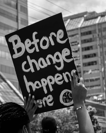 Grayscale photo of person holding banner with " Before the change happens here"
