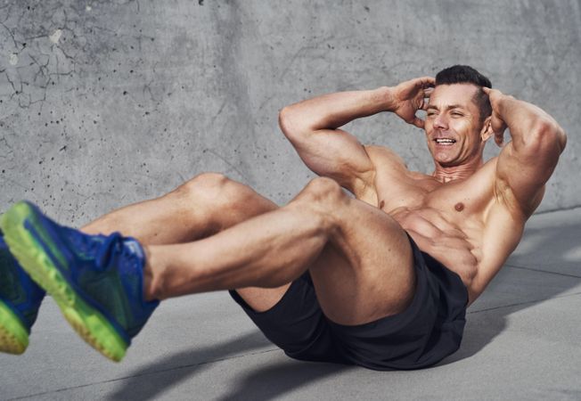 Muscular shirtless man doing ab exercises with grey background