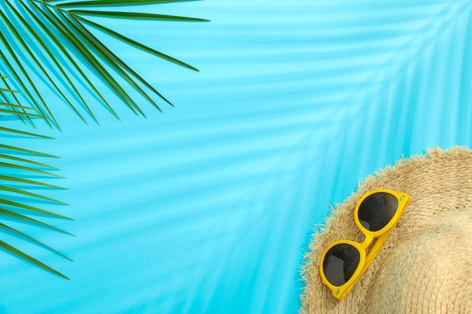 Palm leaves, straw hat and sunglasses on color background, space for text. Summer vacation backdrop