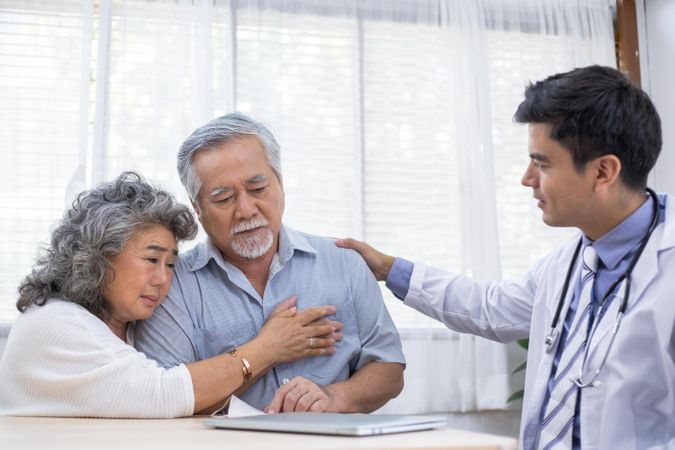 Asian wife embraces mature husband after receiving diagnosis of sickness from doctor