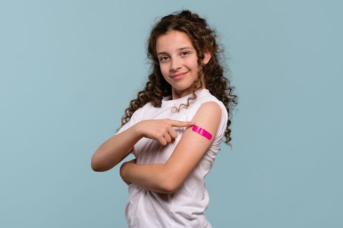 Girl pointing at pink bandage on arm after receiving vaccine.