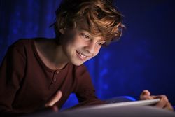 Cheerful boy using tablet in dark room