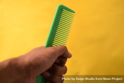 Hand with green hair comb against yellow background bYqwmD