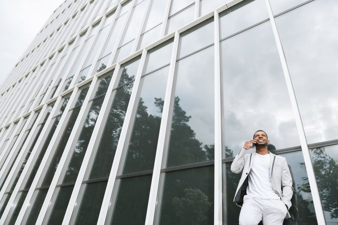 Elegant Black man talking smartphone leaning building