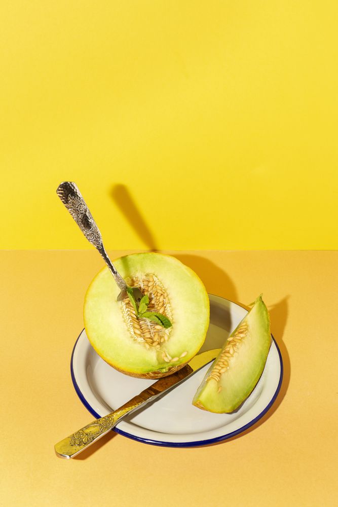 Sliced small melon on plate with spoon and fork