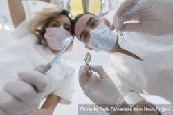Dental colleagues wearing surgical mask while holding angled mirror and drill, ready to begin 4joAJb