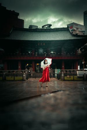 Woman in light top and red skirt holding an umbrella standing beside