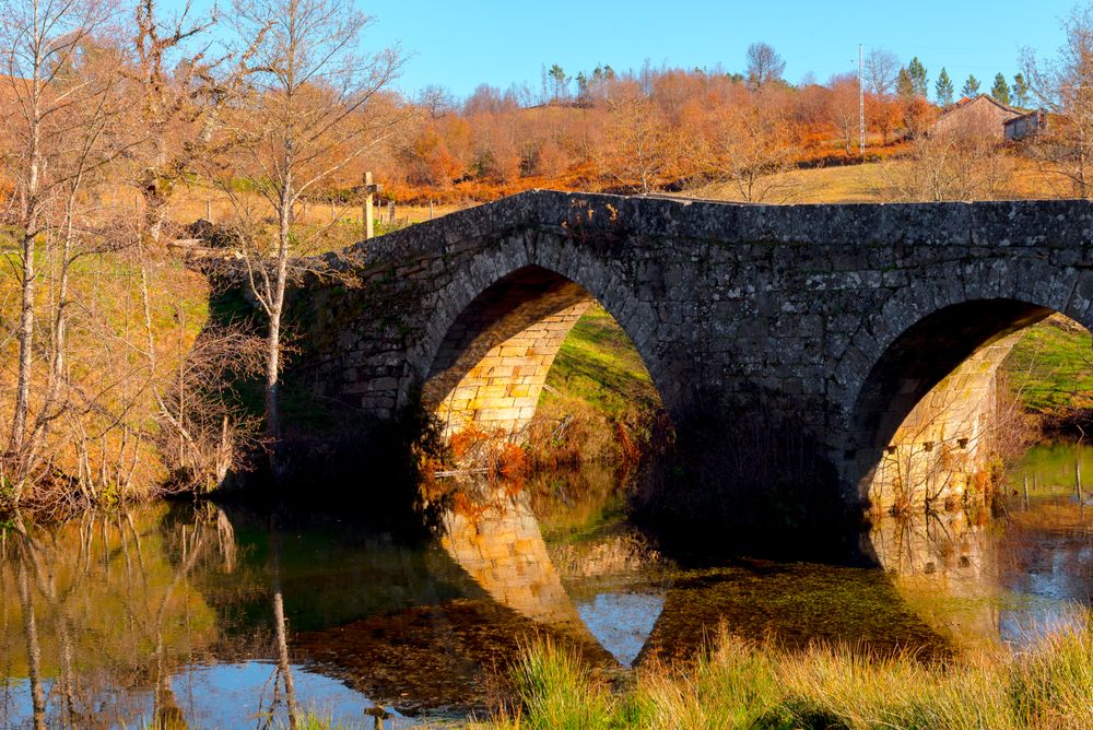 Old bridge over calm river in autumn countryside