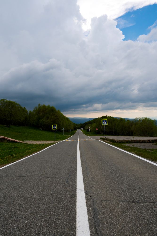 Straight road leading through green landscape under cloudy sky.