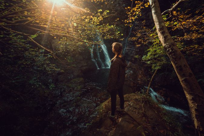 woman standing in a Small river and waterfall flowing in green dark beautiful forest.