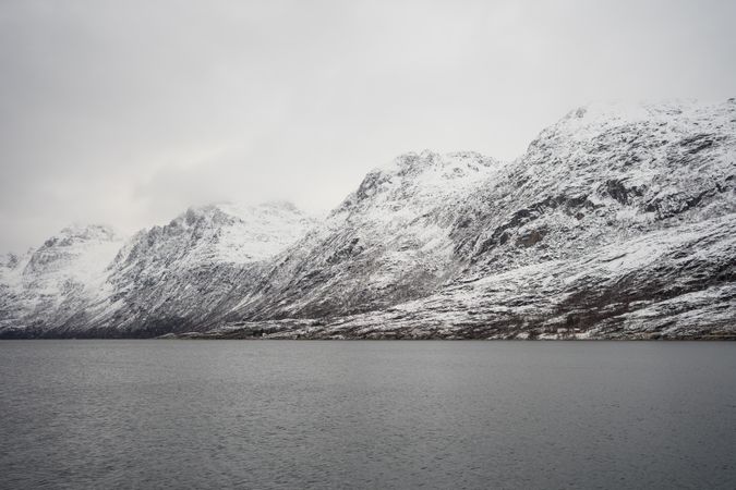 Tranquil lake against snowy hills in cold overcast weather