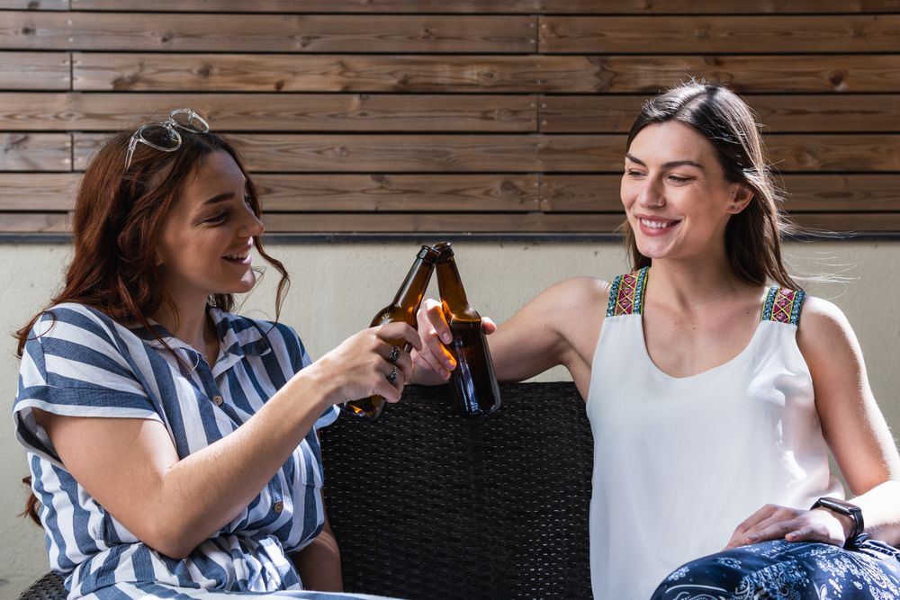 Cheerful girlfriends with beer spending weekend on sofa