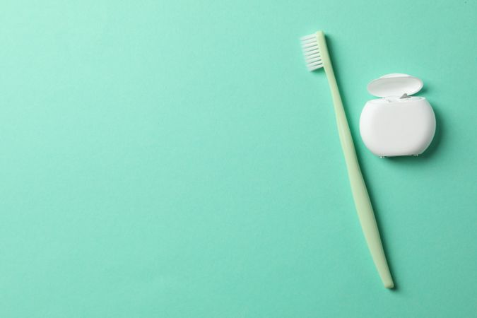 Dental floss and toothbrush on mint background, space for text