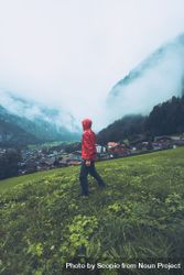 Side view of man in red jacket walking on green grass field near village in Switzerland 0yQ6a0