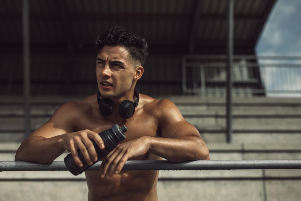 Muscular man holding his water bottle and resting from workout