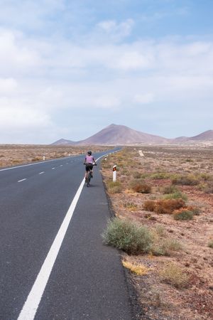 Back of woman biking on quiet paved road