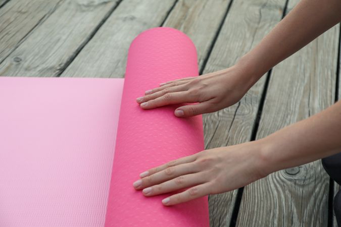 Pink yoga mat and female hands on wooden background, close up