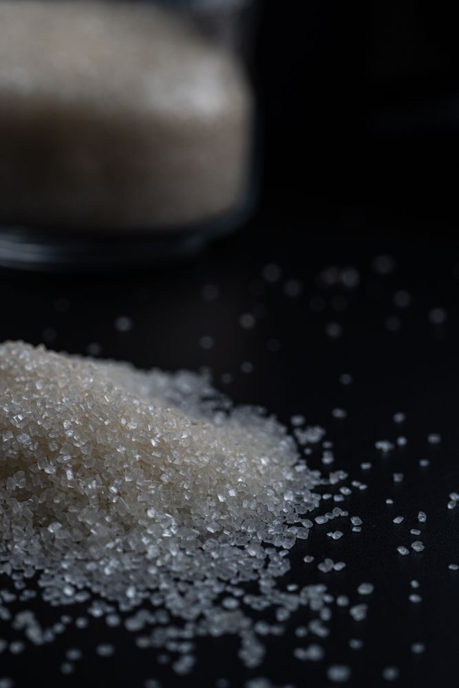 granulated sugar spilling from a glass jar onto a dark surface