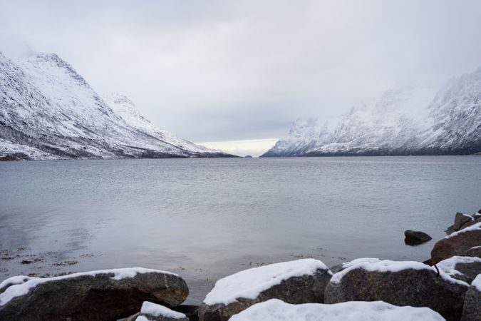 Tranquil lake against snowy hills in cold overcast weather