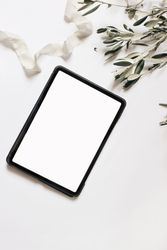 Closeup of tablet with empty screen and olive tree branches and silk ribbon isolated on table